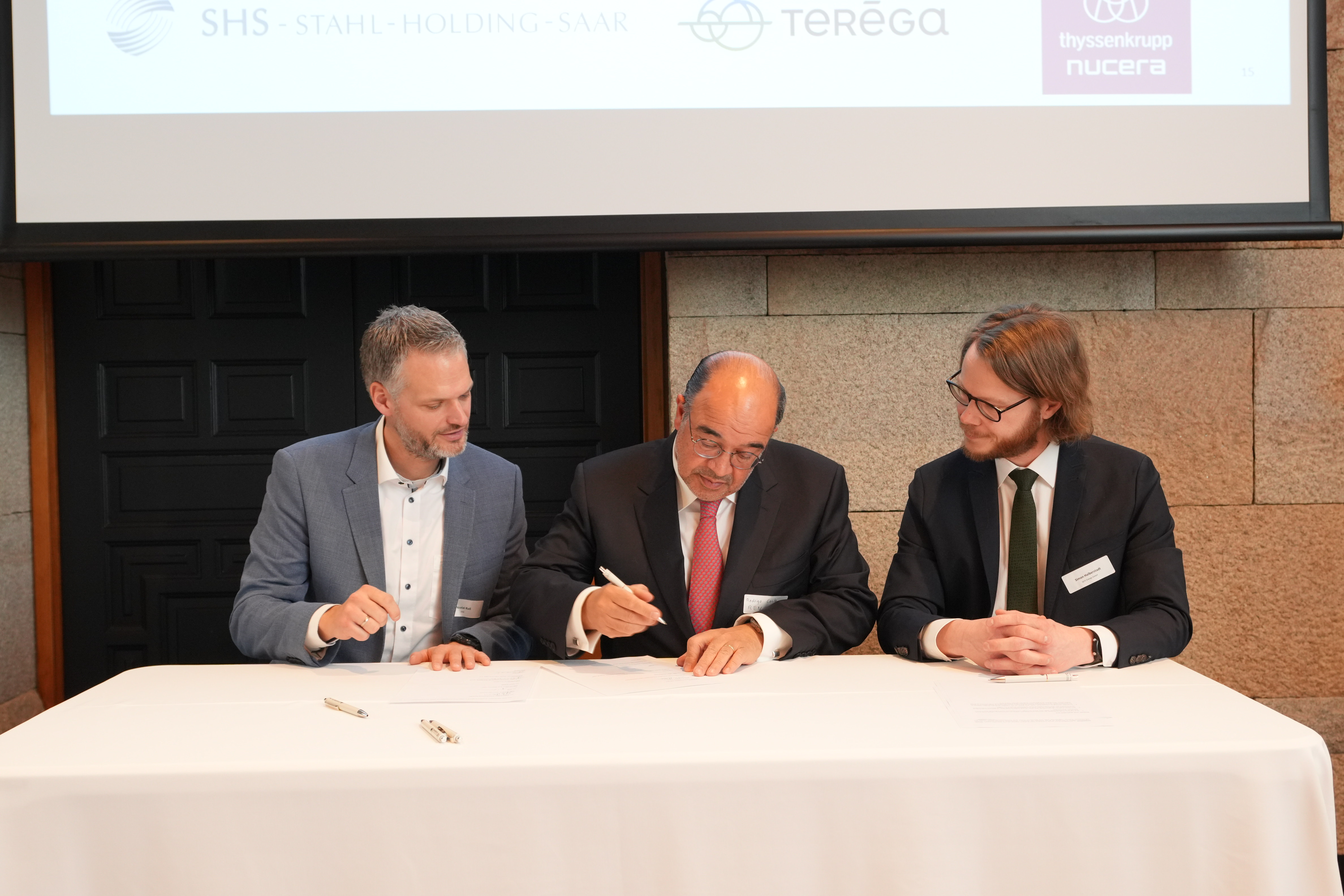 Drei Personen sitzen nebeneinander an einem Tisch.